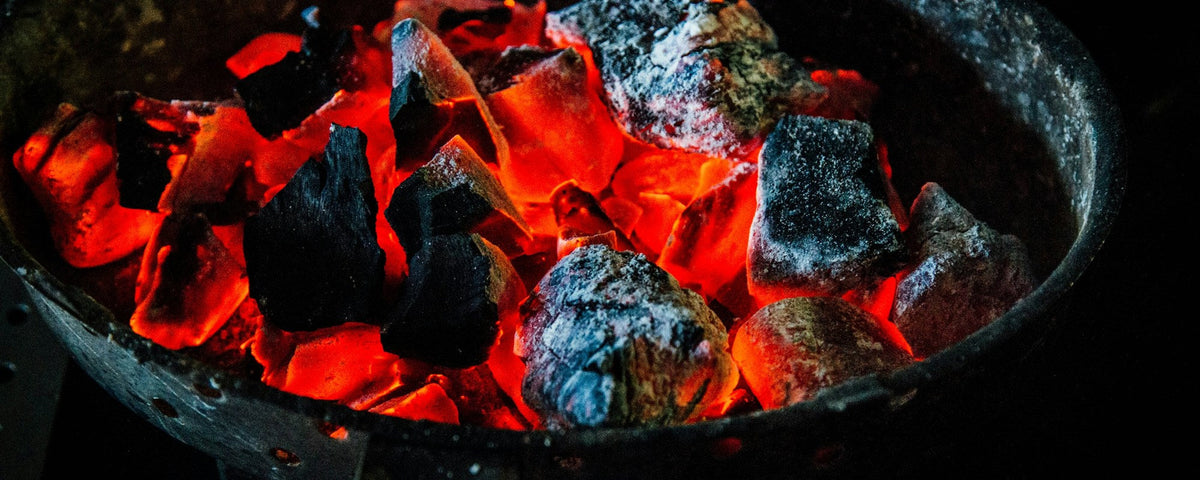 Kamado aansteken: gloeiende stukken houtskool in een ronde kolenmand